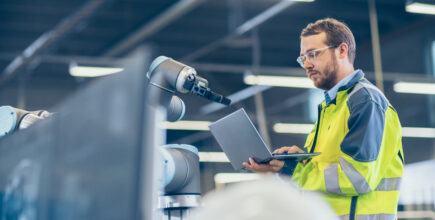 Automation Engineer Uses Laptop for Programming Robotic Arm